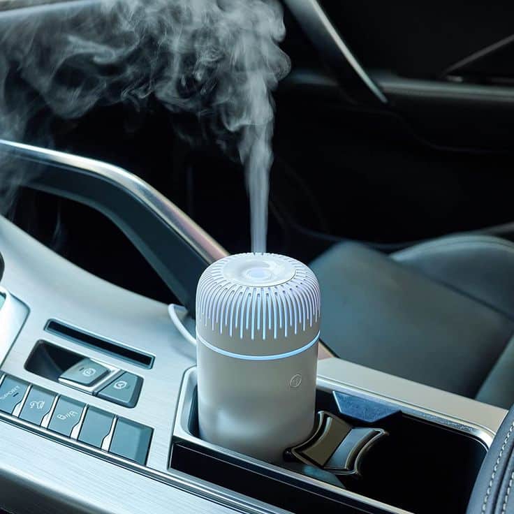 Compact car aroma diffuser emitting mist in cup holder, enhances vehicle air quality.