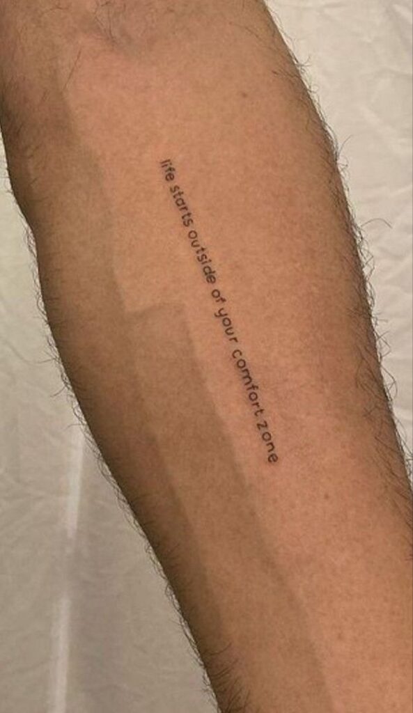 Tattoo on a leg with motivational quote: Life starts outside of your comfort zone, in black ink.