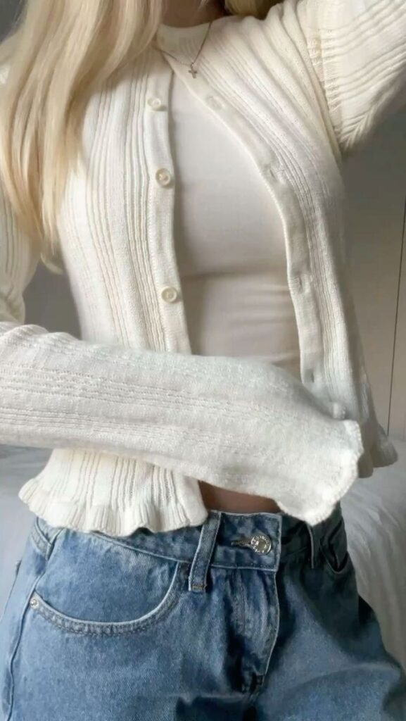 Woman in white knit sweater with blue jeans, showcasing casual fall fashion style.
