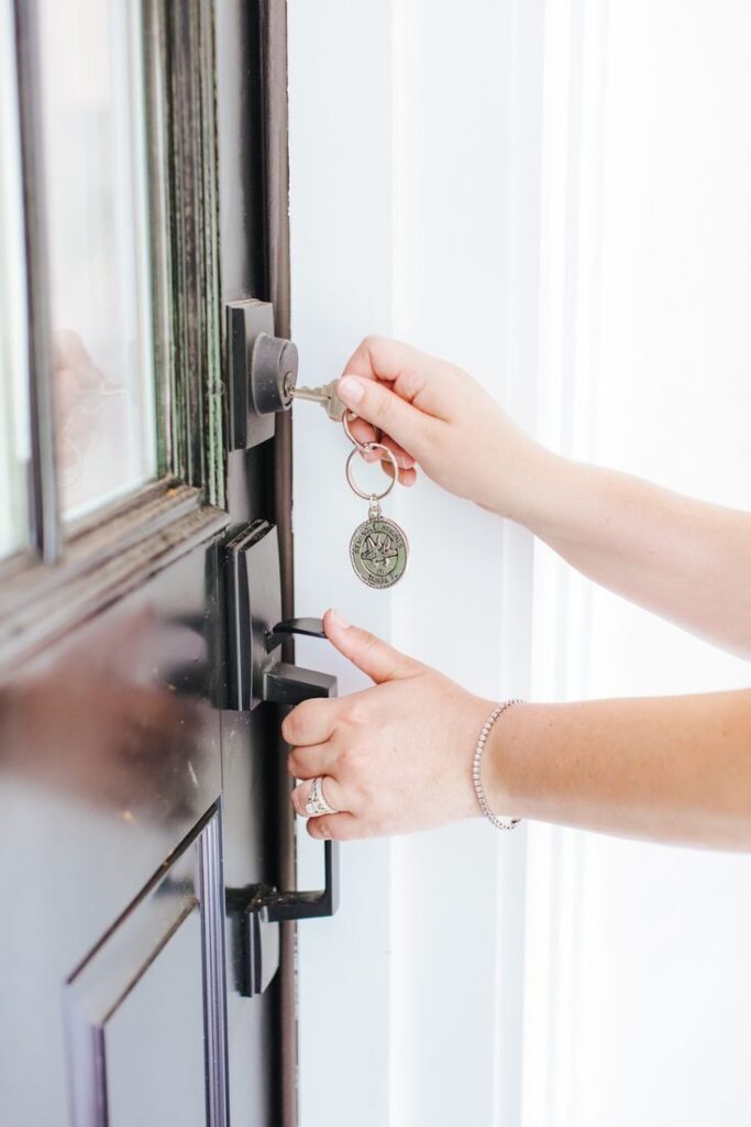 Person unlocking modern black door with key, close-up on hands and keychain.