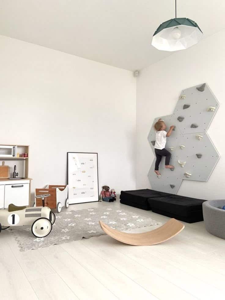 Child climbing indoor wall in modern playroom with toys and soft flooring. Kids Room