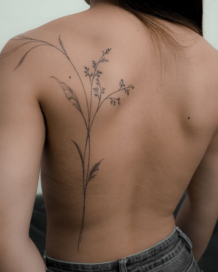 Minimalist floral tattoo on a person's back, showcasing delicate branches and leaves in black ink.