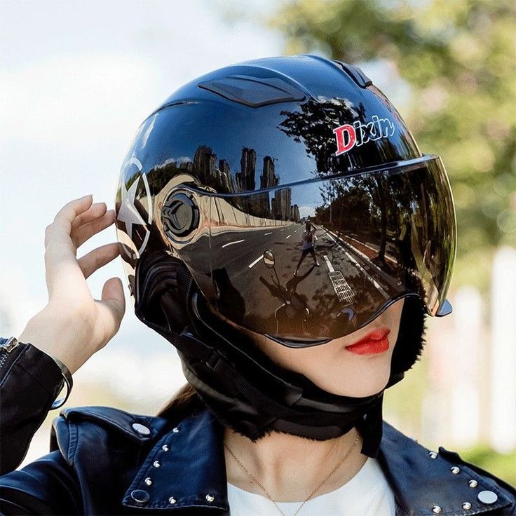 Person in a reflective motorcycle helmet adjusts strap, showing street reflection and cityscape.