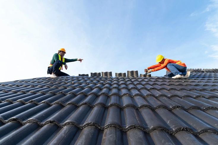 6b6ee7c39e59c8070c707836b6dc240a Roofers installing black tiles on a roof under clear blue sky. Construction workers wearing safety gear and helmets. | Sky Rye Design Roofers installing black tiles on a roof under clear blue sky. Construction workers wearing safety gear and helmets.