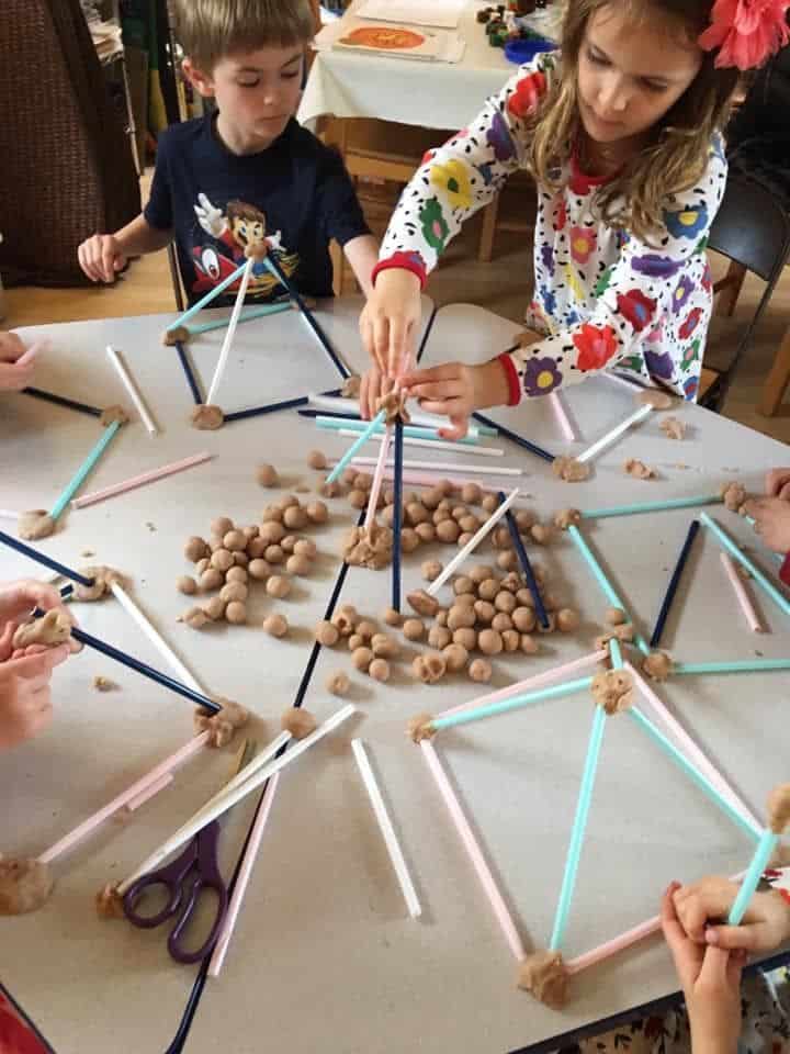 Children building geometric shapes with clay and straws at a table.