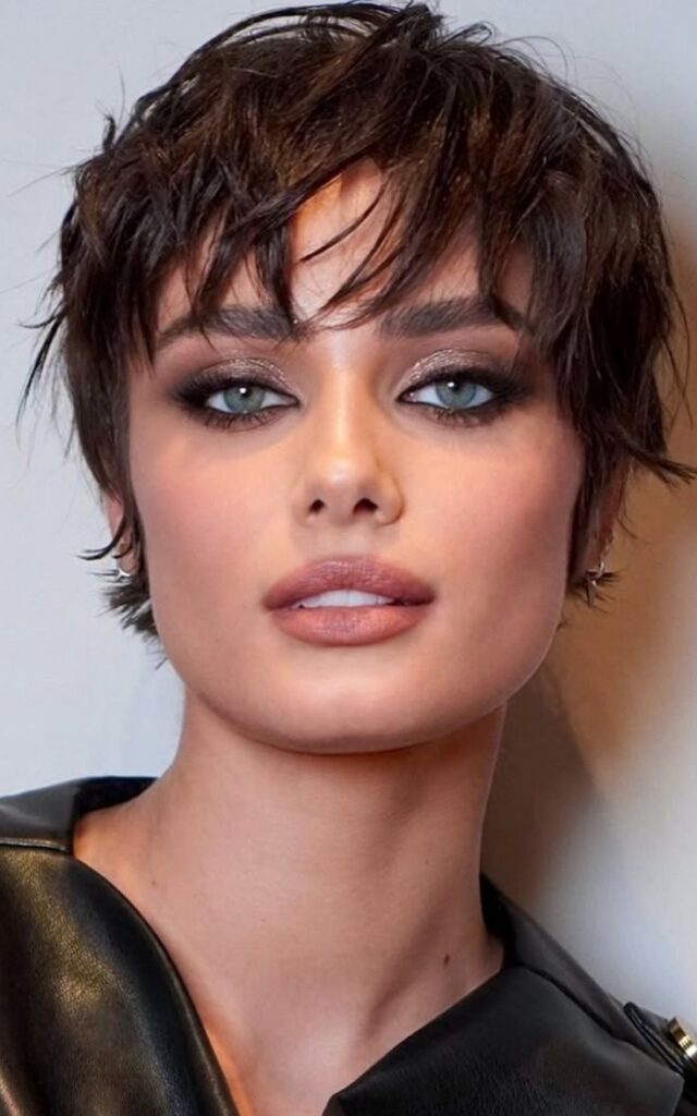 Woman with short dark hair, smoky eye makeup, and glossy lips in a close-up portrait wearing a leather outfit.