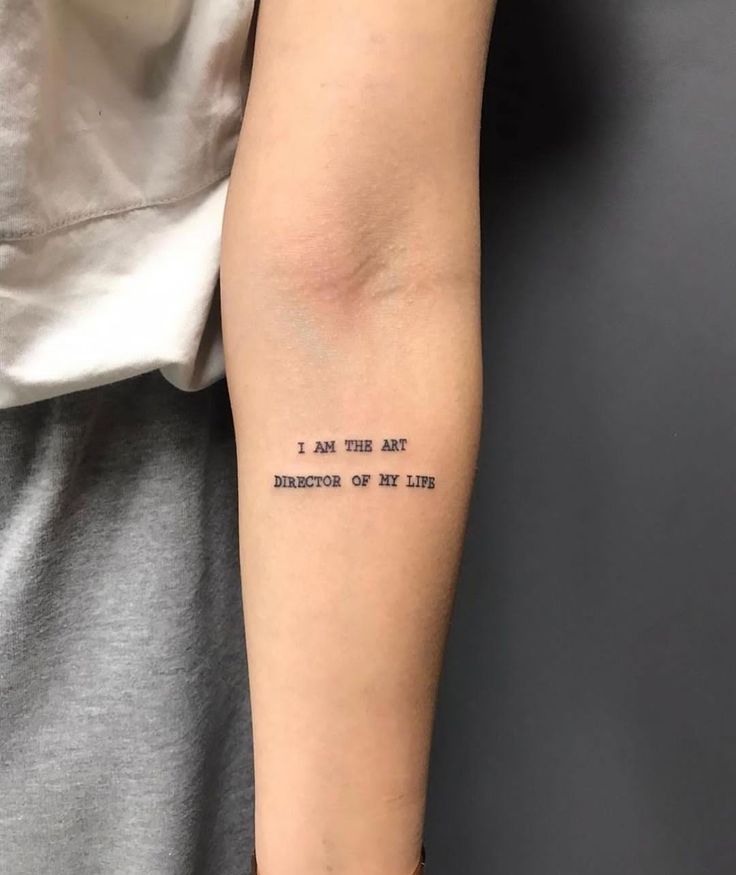 Forearm tattoo reading I am the art director of my life in black ink on light skin, wearing a grey sleeve.