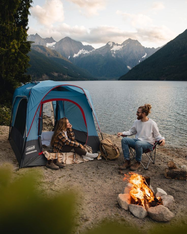 Camping by a mountain lake with a campfire, tent, and friends enjoying nature in a serene landscape.
