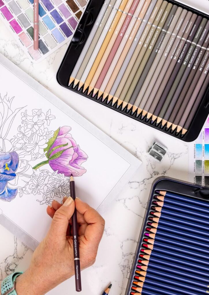Person coloring floral illustration with colored pencils on a marble surface.