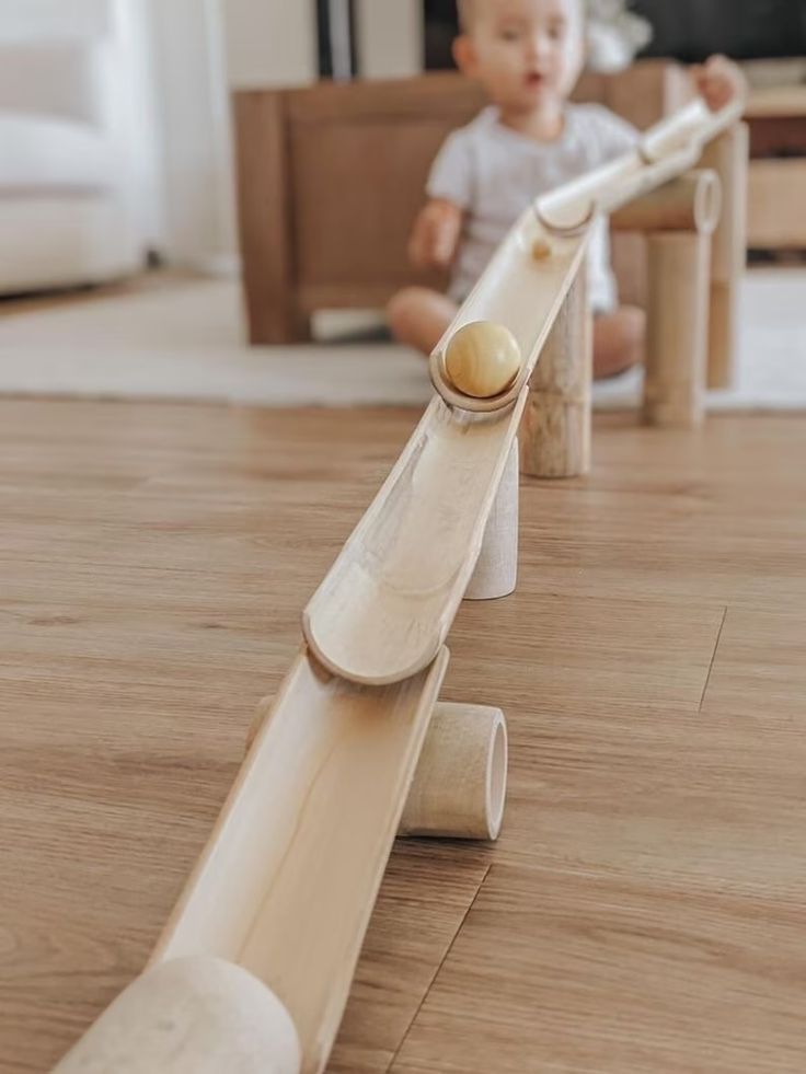 _ 78 Wooden marble run with child playing in background on wooden floor. | Sky Rye Design Wooden marble run with child playing in background on wooden floor.