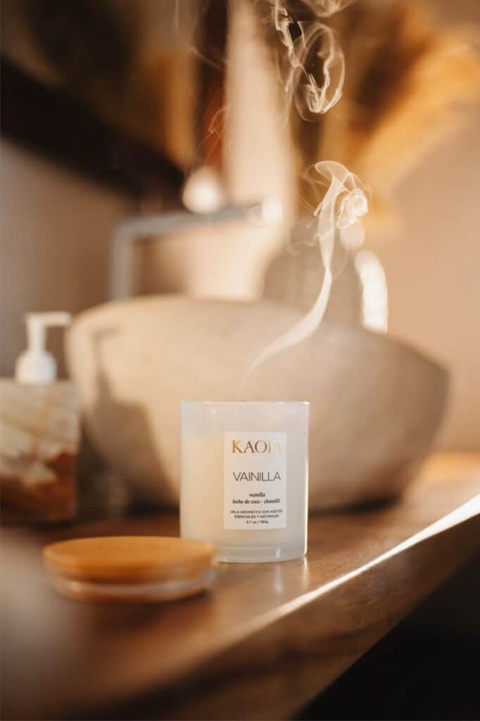 White vanilla-scented candle on wooden table, with smoke rising in a cozy setting.