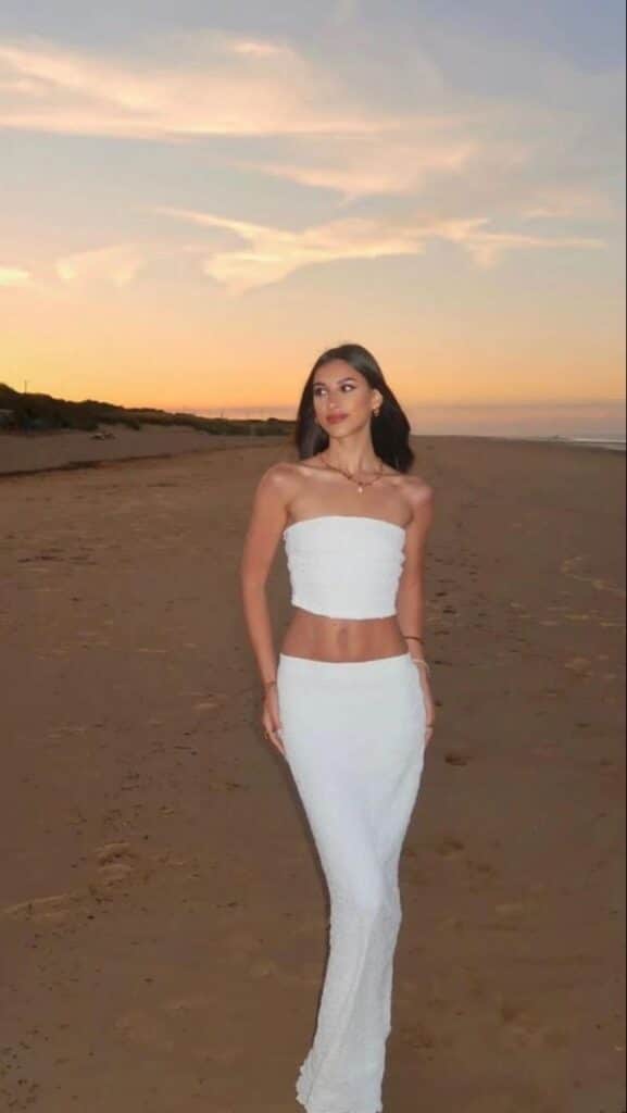 79a984f9-4262-40b9-b9a3-cd3d40b5d5be Woman in white dress walking on a beach at sunset, serene atmosphere. | Sky Rye Design Woman in white dress walking on a beach at sunset, serene atmosphere.