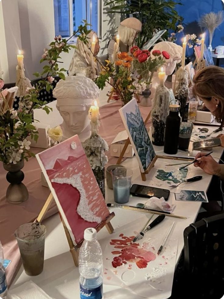 Art class with easels, paint palettes, and sculptures surrounded by flowers and candles. Serene indoor painting session.