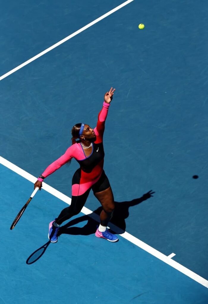 Tennis player in vibrant outfit serving on a blue court, showcasing athletic strength and precision.