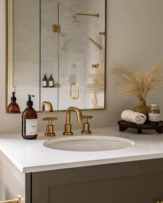 Elegant bathroom with gold fixtures, mirrored cabinet, and stylish decor on a modern countertop.