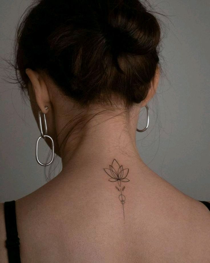 Minimalist lotus flower tattoo on the back of a woman's neck, styled with hoop earrings and an updo.