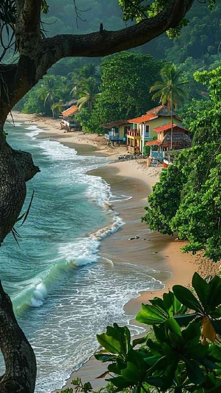 Tropical beach with lush greenery, colorful houses, and gentle waves under a sunny sky, framed by tree branches.