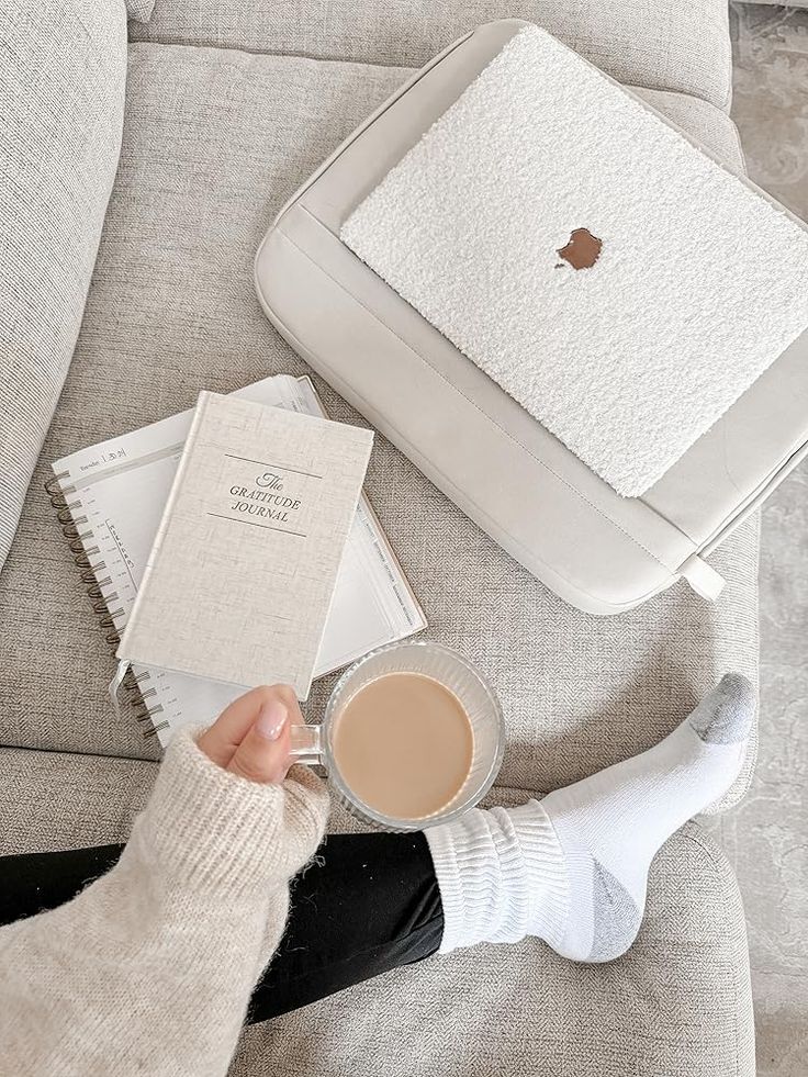81a11a37-7815-4d8e-82c1-062c089951a2 Cozy scene with a person holding a coffee on a sofa, alongside a journal, laptop, and planner. Perfect for relaxation and work. | Sky Rye Design Cozy scene with a person holding a coffee on a sofa, alongside a journal, laptop, and planner. Perfect for relaxation and work.