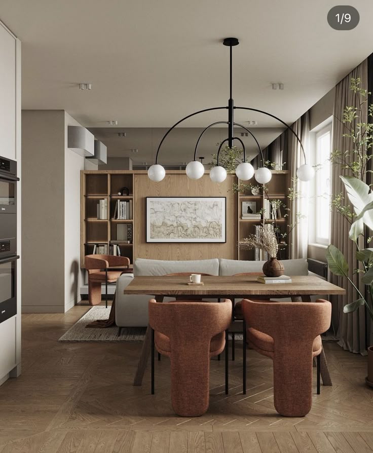 Modern living room with elegant chandelier, wooden table, orange chairs, cozy sofa, and natural light from large windows.