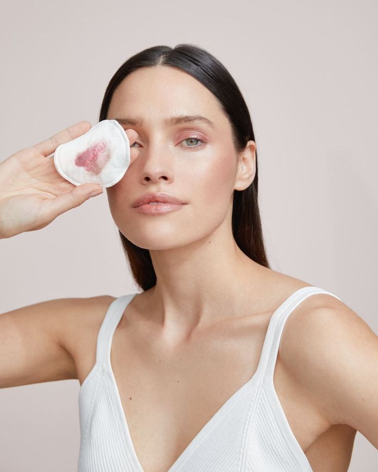 Woman using a cotton pad for makeup removal, wearing a white tank top, skincare routine concept.