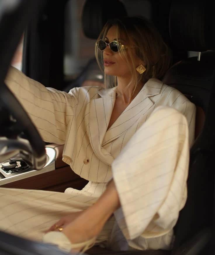 Stylish woman in striped suit and sunglasses sitting in car, looking chic and confident.