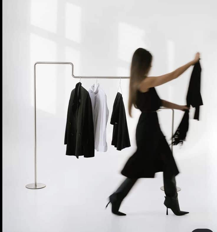 Woman in motion near minimalist clothing rack with black and white garments, on a bright, modern background.