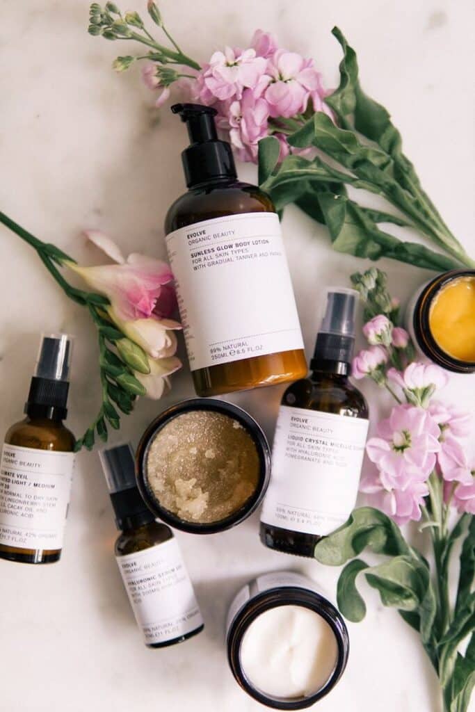 Evolve Organic Beauty skincare products with pink flowers on marble background.