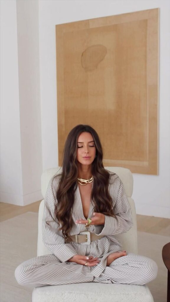 Woman meditating in stylish loungewear, sitting cross-legged in a minimalistic room with neutral decor.