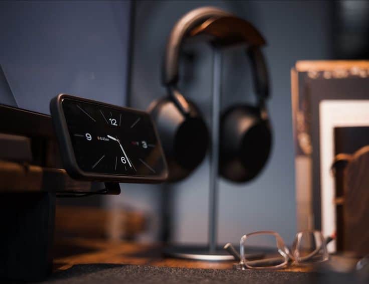 Smartphone on stand showing time near headphones and glasses, creating a modern desk setup ambiance.
