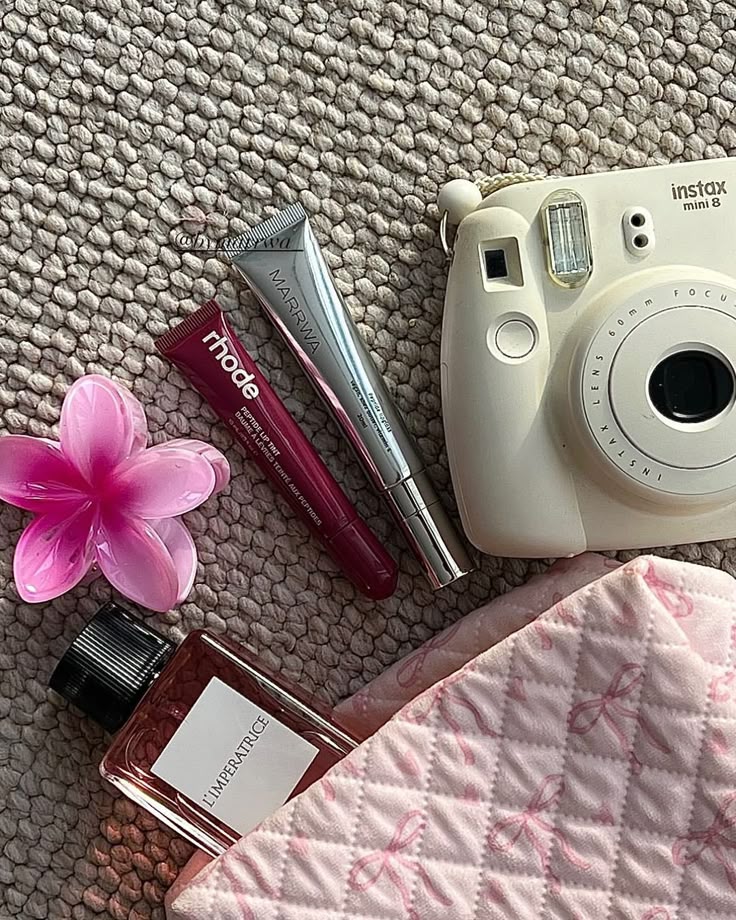 8d625586-4f48-4371-9da9-d3ac010b1afe Flat lay of Instax camera, lip gloss tubes, perfume, pink flower, and quilted fabric on a textured surface. | Sky Rye Design Flat lay of Instax camera, lip gloss tubes, perfume, pink flower, and quilted fabric on a textured surface.
