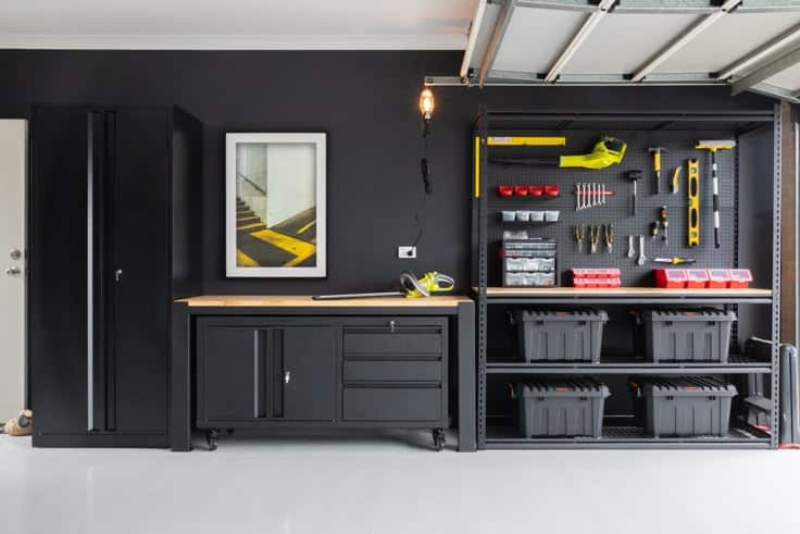 Organized garage workspace with black cabinets, hanging tools, and storage bins on shelving unit. Efficient and tidy setup.
