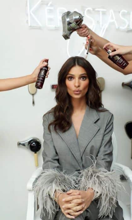 Woman in a stylish gray suit with feather cuffs getting her hair styled with blow dryers and hair products.