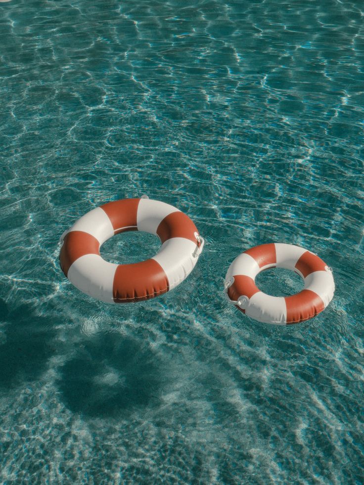 Two striped lifebuoys float on clear, rippling pool water, creating a sense of relaxation and safety.