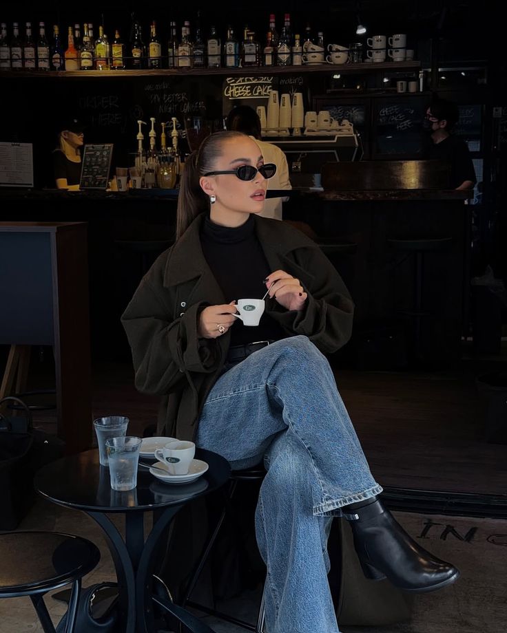 Woman enjoying coffee at a stylish cafe, wearing sunglasses and casual chic attire.