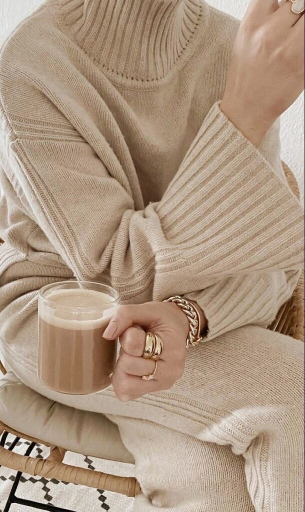 Cozy beige sweater outfit with gold jewelry, holding a cup of coffee.
