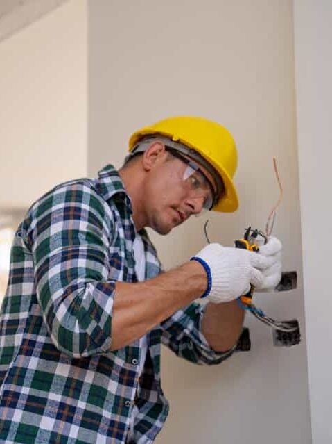 960x0 Electrician wearing helmet and gloves wiring a socket indoors, ensuring safety and precision in electrical installation. | Sky Rye Design Electrician wearing helmet and gloves wiring a socket indoors, ensuring safety and precision in electrical installation.