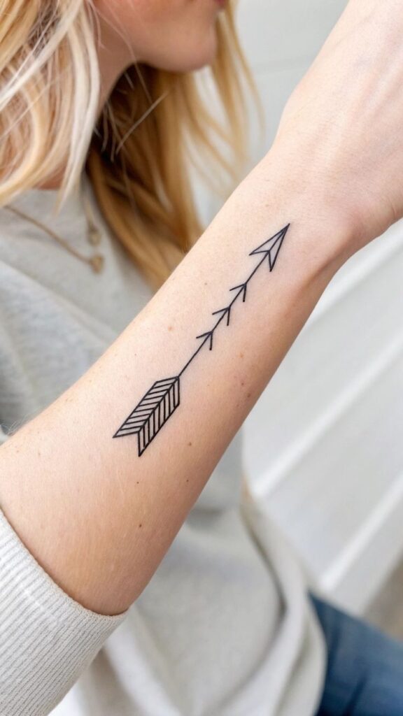 Minimalistic arrow tattoo on a forearm with person in light gray sweater.