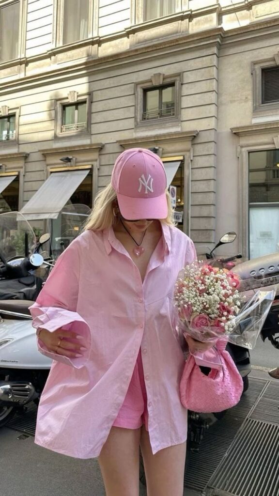 Person in pink outfit and cap holding a bouquet on a city street, standing beside scooters.