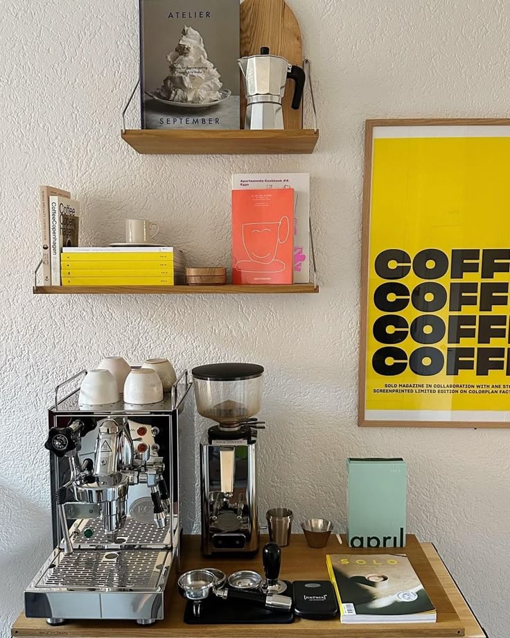 Home coffee bar setup with espresso machine, grinder, books, and art on a wooden shelf. Cozy and stylish decor.