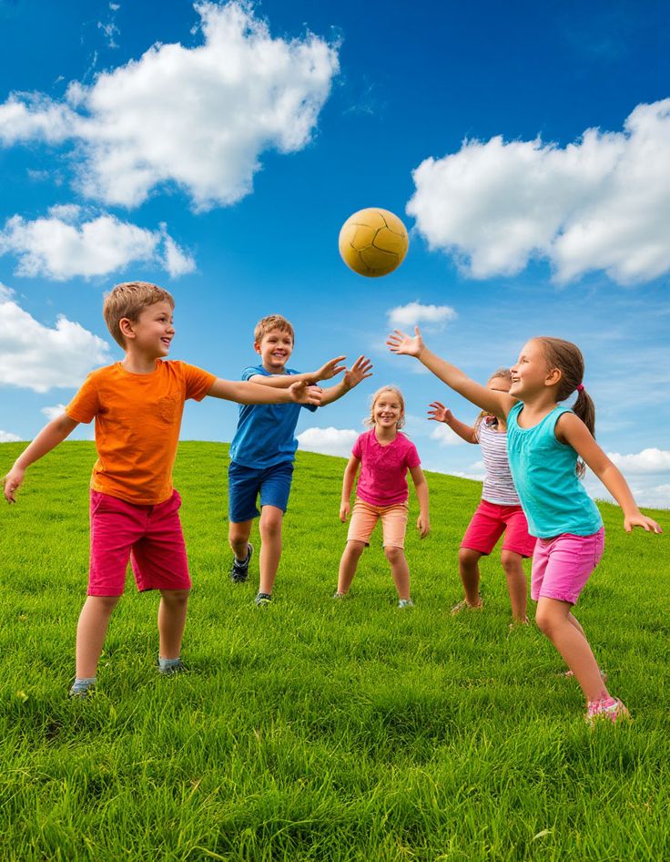 Children playing with a ball on a grassy field under a blue sky with clouds, enjoying outdoor activities in summer.