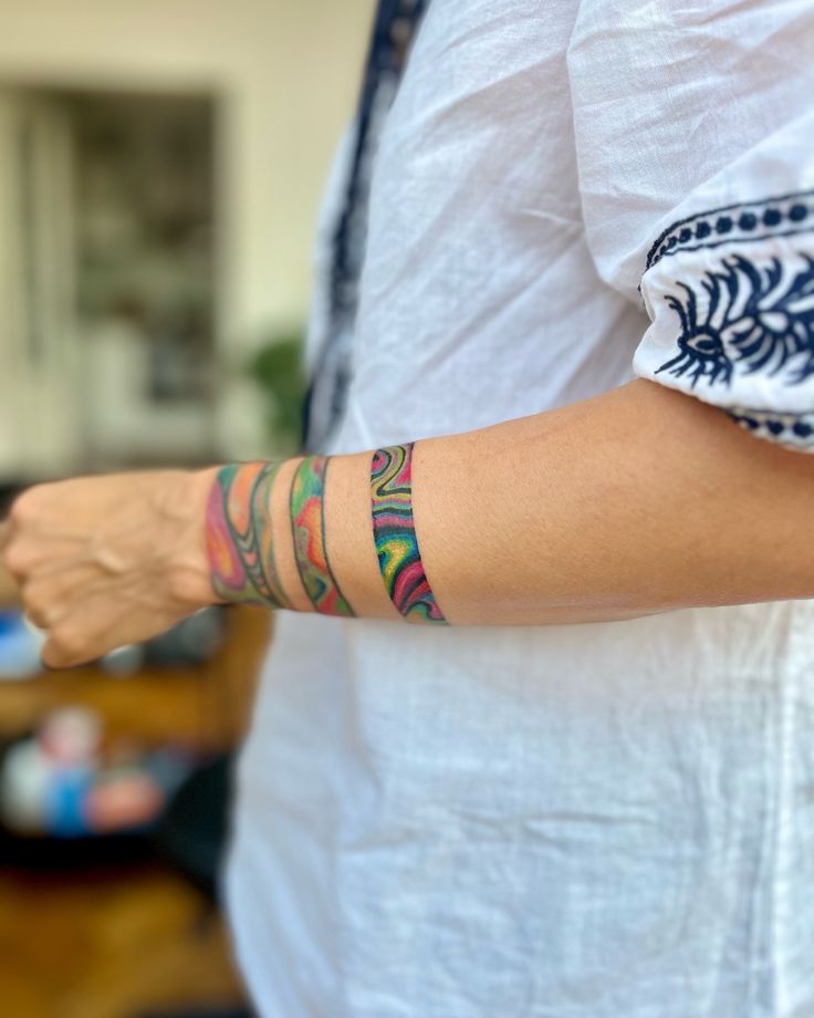 Colorful abstract band tattoo on person's forearm, wearing a white shirt with blue patterns.
