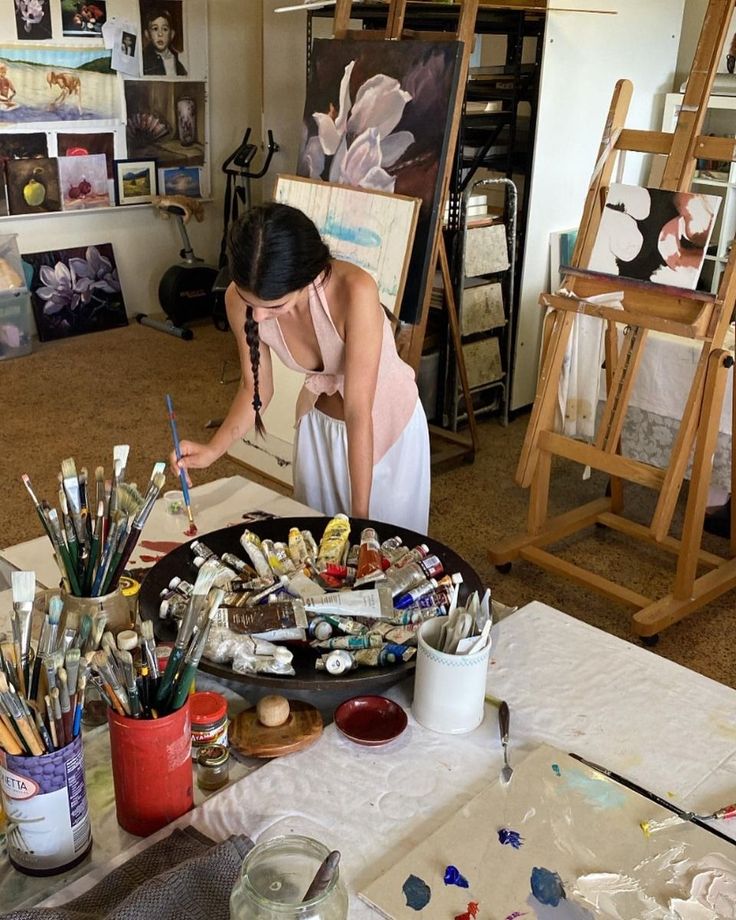 Artist painting in a studio filled with supplies and canvases, creating colorful artwork in a creative space.