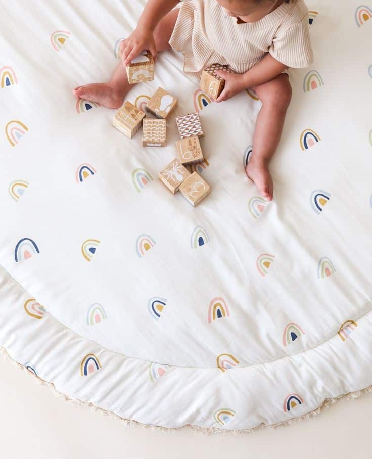 Baby playing with wooden blocks on a rainbow-patterned blanket.