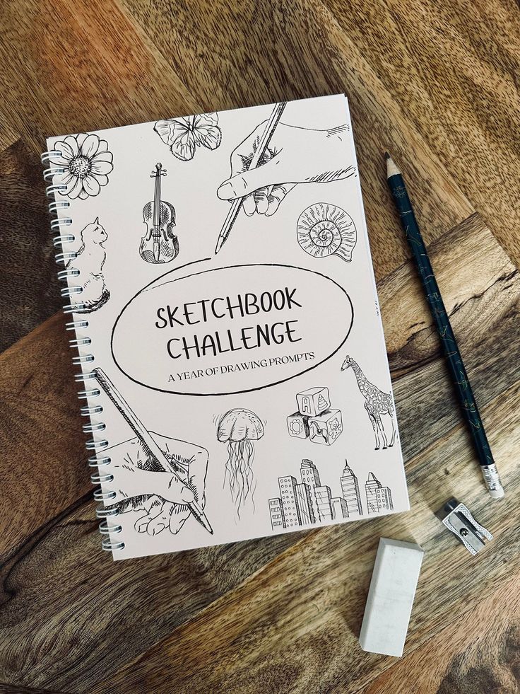 Sketchbook with drawing prompts, featuring illustrations of a hand, violin, giraffe, and cityscape, on a wooden table.