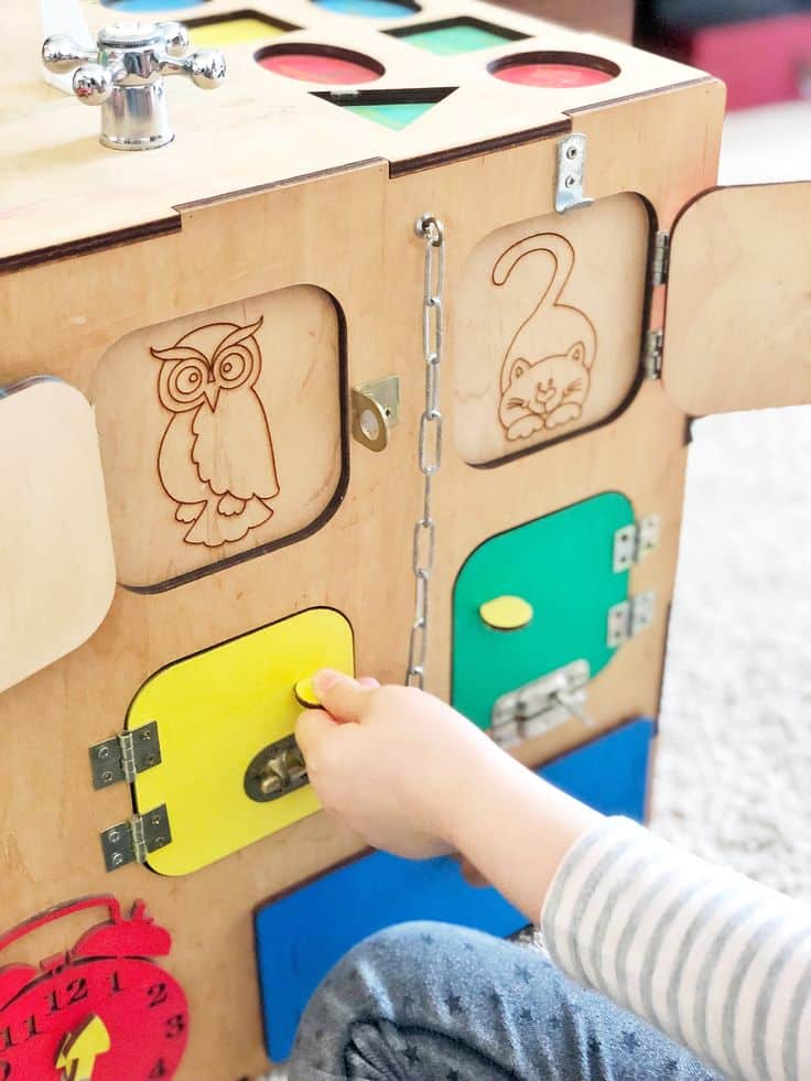 Child playing with a wooden activity board featuring animal engravings and colorful doors.