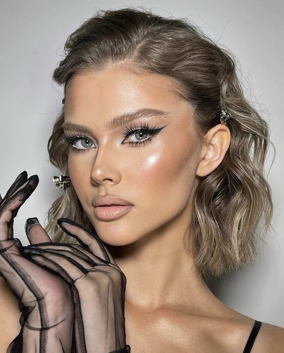 Woman with styled hair and dramatic makeup, wearing sheer black gloves, showcasing a glamorous look.