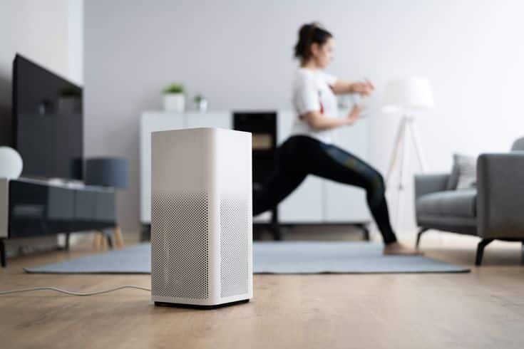 Air purifier operating in modern living room while person practices yoga on mat in the background.