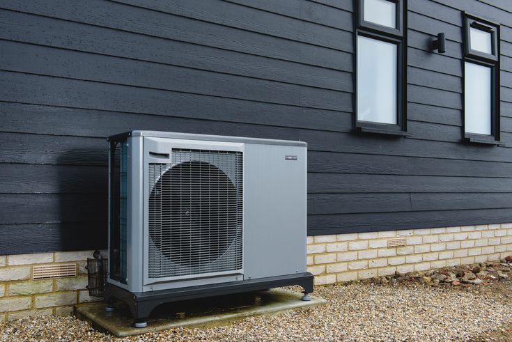 Outdoor heat pump unit against a modern black exterior wall, highlighting energy-efficient home heating.