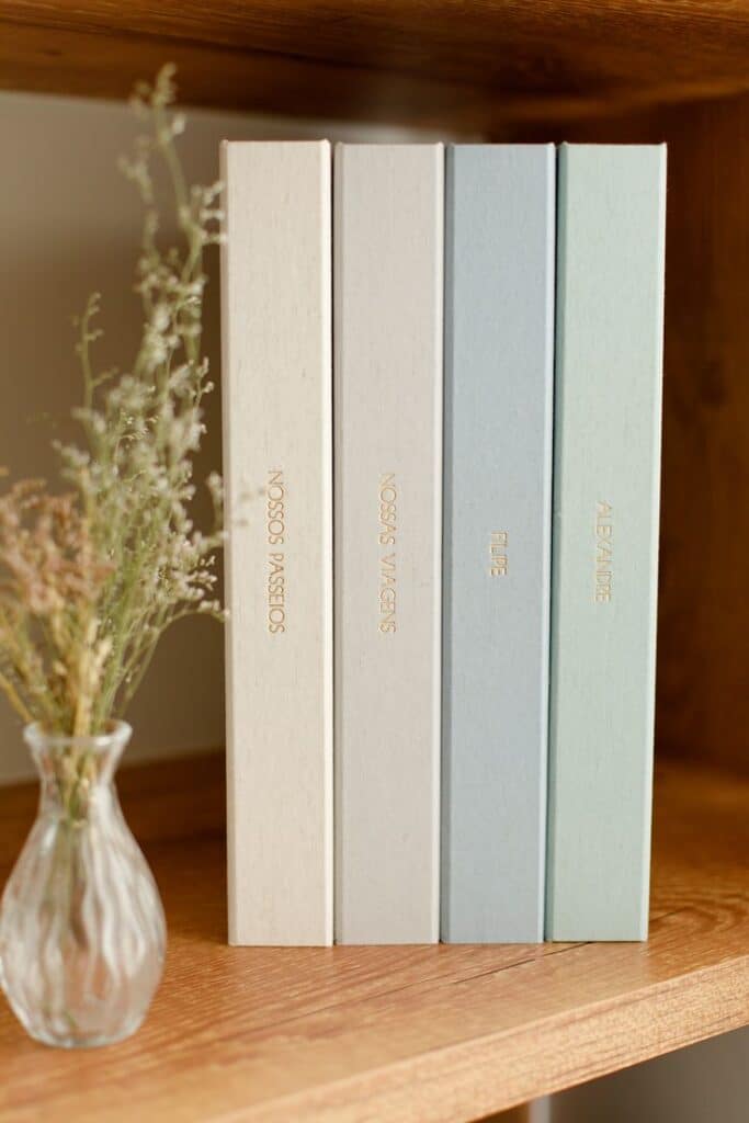 Decorative books on a wooden shelf with a vase of dried flowers, creating a cozy, minimalist aesthetic.