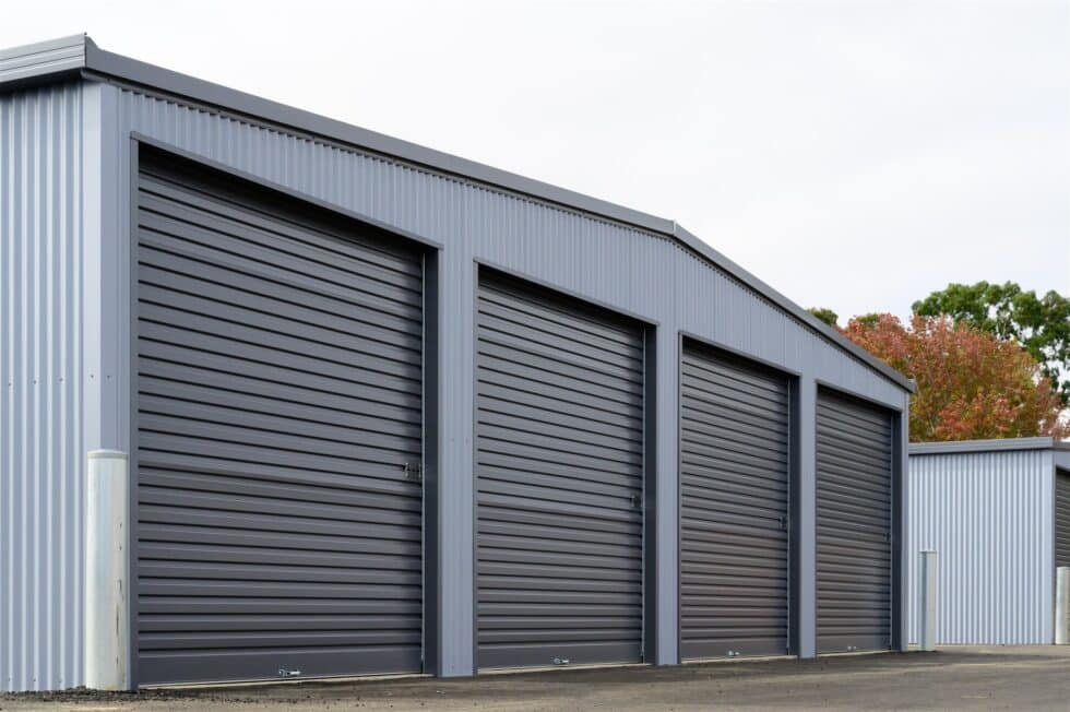 Large gray corrugated metal storage units with closed roller doors, outdoor perspective of industrial building.